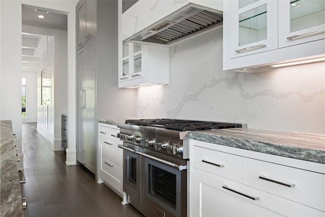 kitchen with backsplash, range with two ovens, light stone counters, glass insert cabinets, and custom range hood