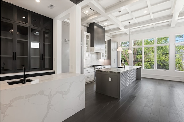 kitchen with high end range, a sink, beamed ceiling, dark cabinetry, and extractor fan