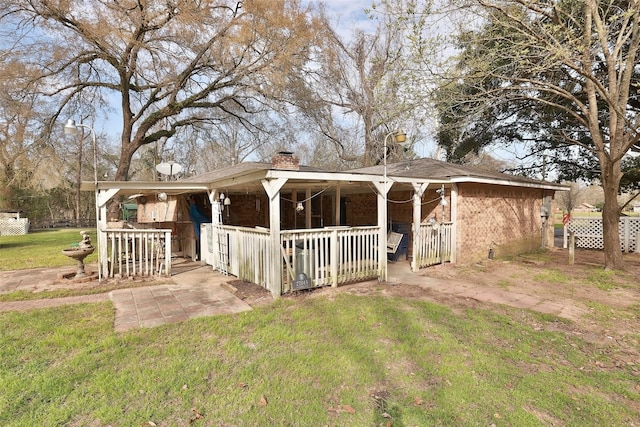 view of front of property featuring brick siding, a chimney, a porch, and a front lawn