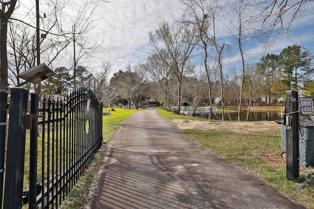 view of street with driveway, a water view, and a gated entry