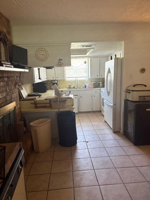 kitchen with a textured ceiling, white cabinetry, light tile patterned floors, a sink, and white appliances