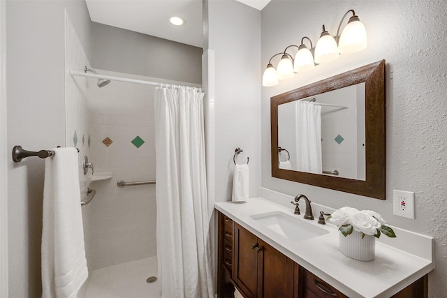 bathroom with a textured wall, vanity, and tiled shower