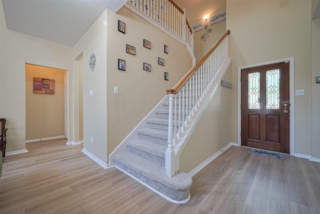 foyer entrance with stairway, wood finished floors, a towering ceiling, and baseboards