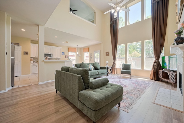 living room with recessed lighting, ceiling fan, light wood finished floors, and a towering ceiling