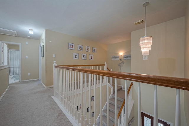 hallway featuring an upstairs landing, visible vents, baseboards, carpet floors, and attic access