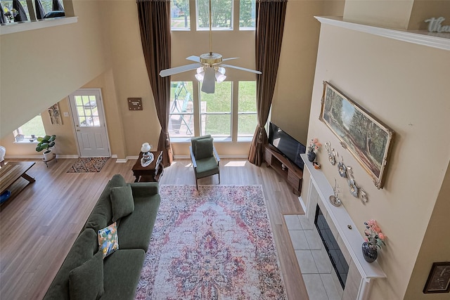living area featuring light wood-type flooring, a towering ceiling, a ceiling fan, and baseboards