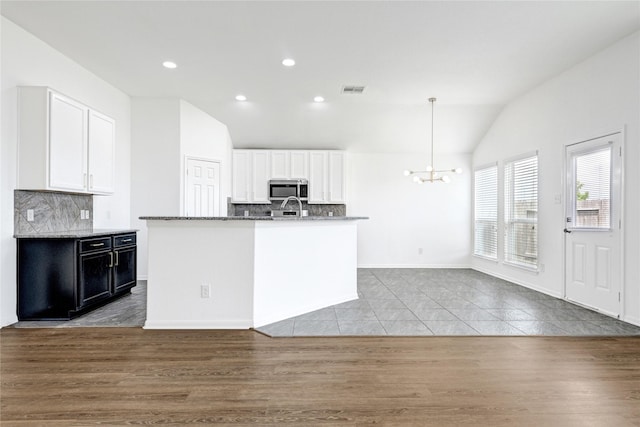 kitchen with stainless steel microwave, decorative backsplash, vaulted ceiling, and white cabinetry
