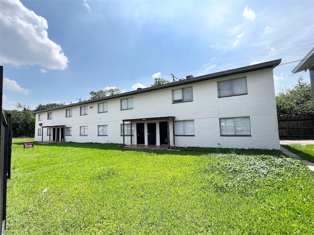 back of property with brick siding, fence, french doors, and a lawn