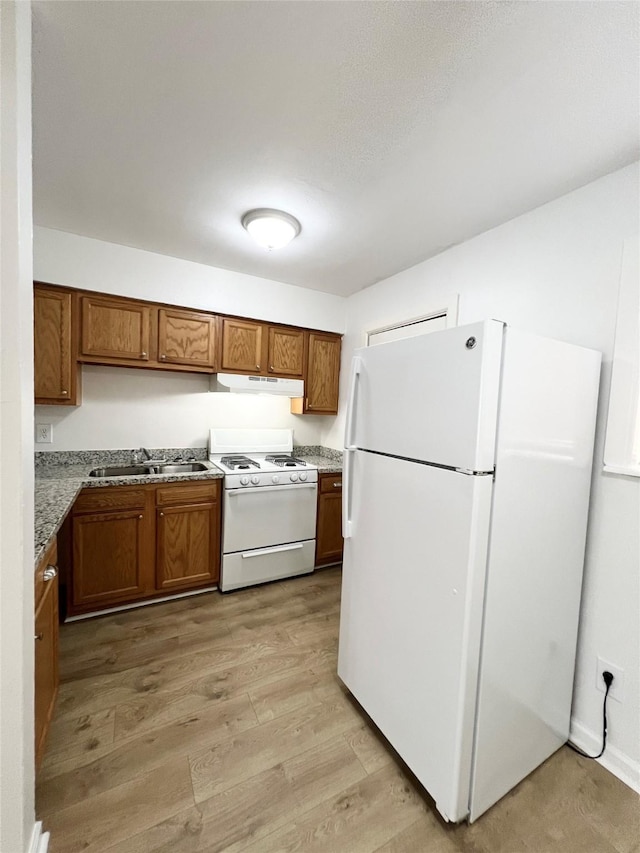 kitchen featuring brown cabinetry, white appliances, under cabinet range hood, and a sink