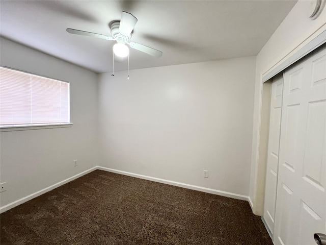 unfurnished bedroom featuring baseboards, dark carpet, a ceiling fan, and a closet