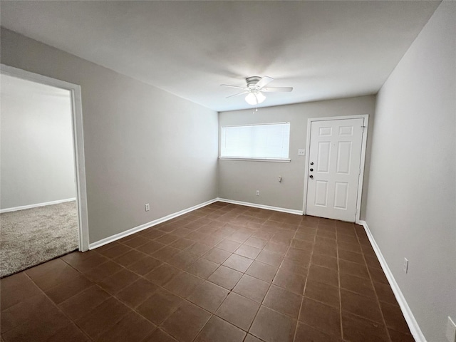 empty room with ceiling fan, dark tile patterned floors, and baseboards