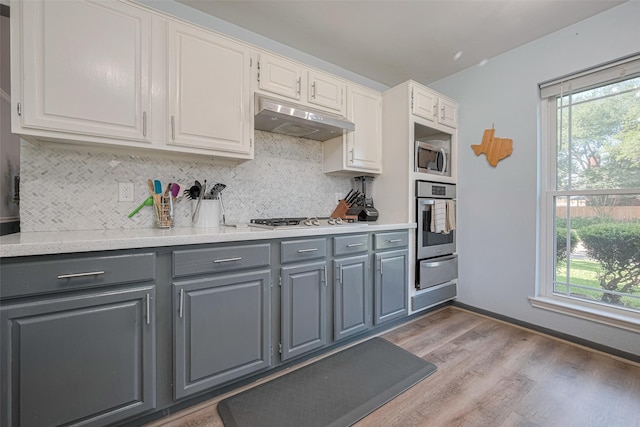 17022 Shadow Valley Dr, Spring, TX 77379 - kitchen featuring appliances with stainless steel finishes, gray cabinets, under cabinet range hood, light wood-type flooring, and tasteful backsplash