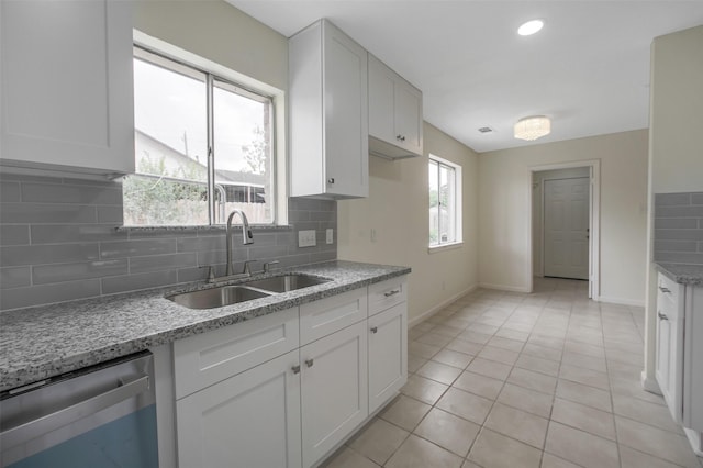 kitchen with light stone counters, a sink, baseboards, decorative backsplash, and stainless steel dishwasher