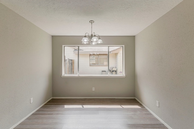 unfurnished dining area with a chandelier, wood finished floors, a textured ceiling, and a textured wall