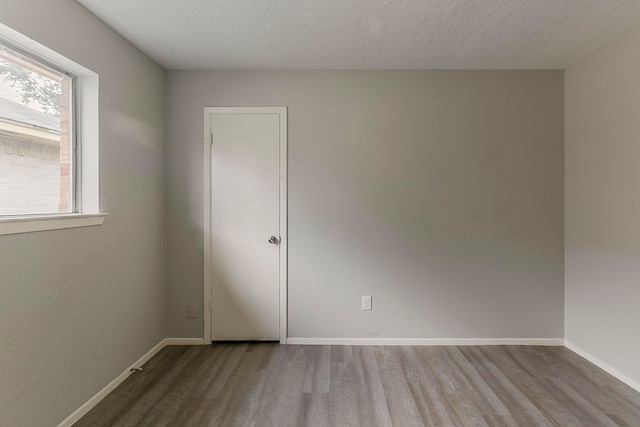 spare room with a textured ceiling, wood finished floors, and baseboards