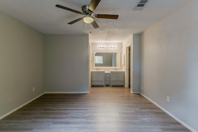 unfurnished bedroom with a textured ceiling, connected bathroom, visible vents, baseboards, and wood finished floors