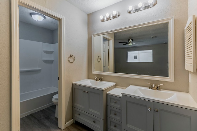 full bathroom with a sink, two vanities, toilet, wood finished floors, and a ceiling fan