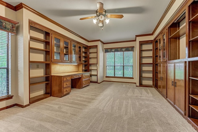 unfurnished office featuring ornamental molding, built in desk, light carpet, and ceiling fan