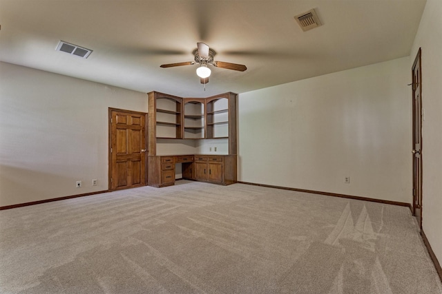 empty room featuring built in study area, light colored carpet, and visible vents