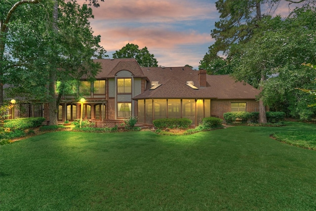 view of front of property featuring brick siding, a chimney, a yard, and a sunroom