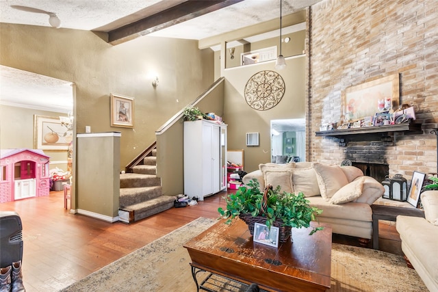 living room featuring wood finished floors, stairs, beamed ceiling, a brick fireplace, and a high ceiling
