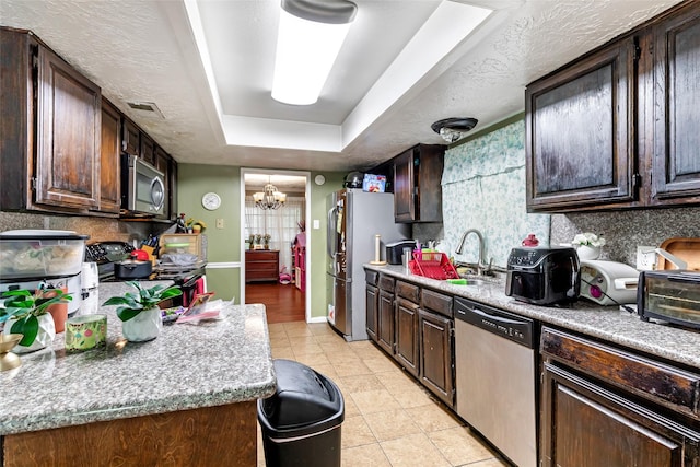 kitchen featuring a sink, a raised ceiling, stainless steel appliances, dark brown cabinetry, and an inviting chandelier