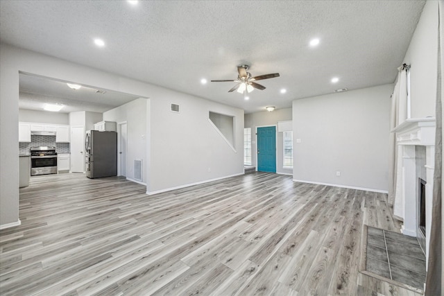 unfurnished living room featuring light wood-style floors, a fireplace, visible vents, a ceiling fan, and a textured ceiling