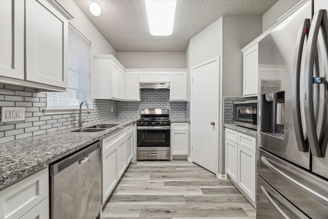 kitchen with a sink, backsplash, a textured ceiling, white cabinets, and appliances with stainless steel finishes