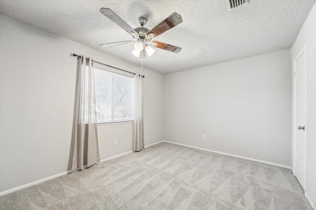 empty room featuring a ceiling fan, visible vents, light carpet, baseboards, and a textured ceiling