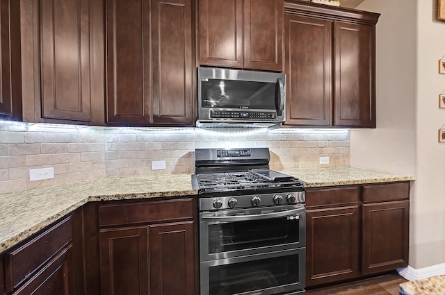 kitchen featuring light stone countertops, dark brown cabinets, backsplash, and appliances with stainless steel finishes