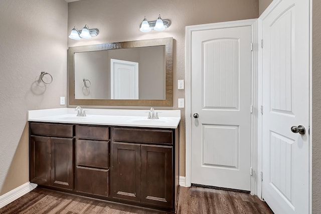 bathroom featuring double vanity, a sink, wood finished floors, and baseboards