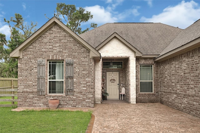 view of front of home featuring fence, a patio area, a shingled roof, and brick siding