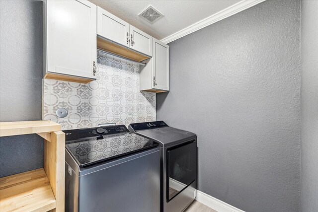 clothes washing area with washer and dryer, a textured wall, light wood finished floors, visible vents, and ornamental molding