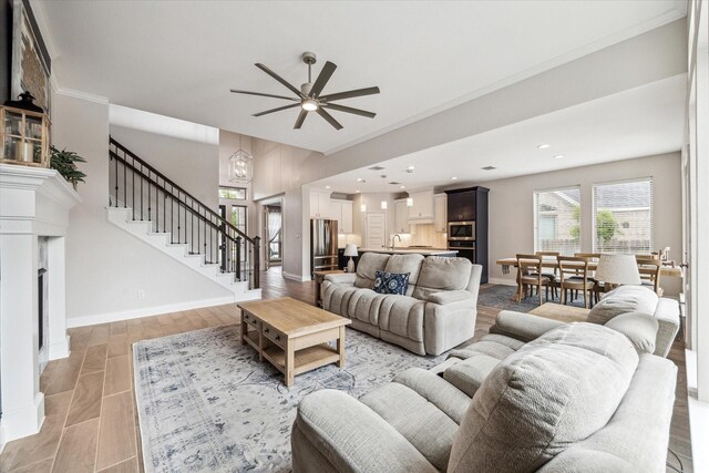 living area featuring a fireplace, light wood-style flooring, a ceiling fan, baseboards, and stairway