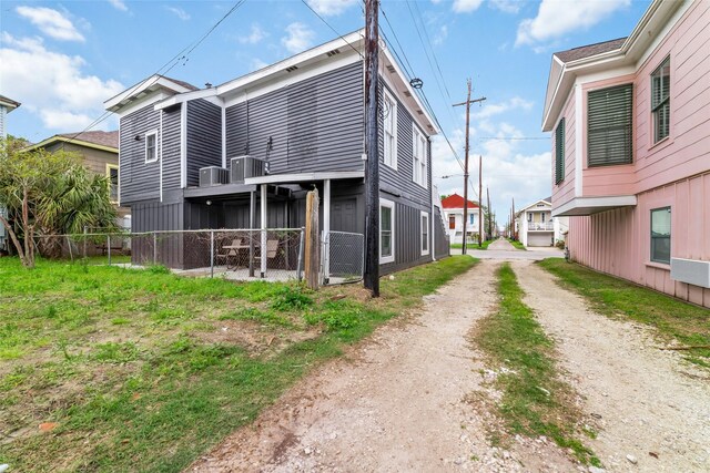 back of house with fence, dirt driveway, and central air condition unit