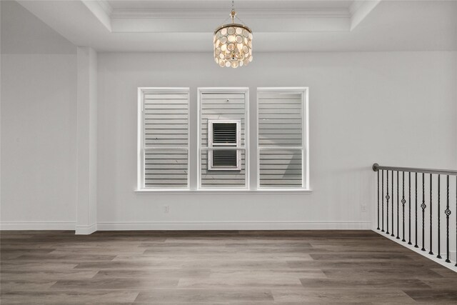 unfurnished dining area with a notable chandelier, a raised ceiling, baseboards, ornamental molding, and wood finished floors