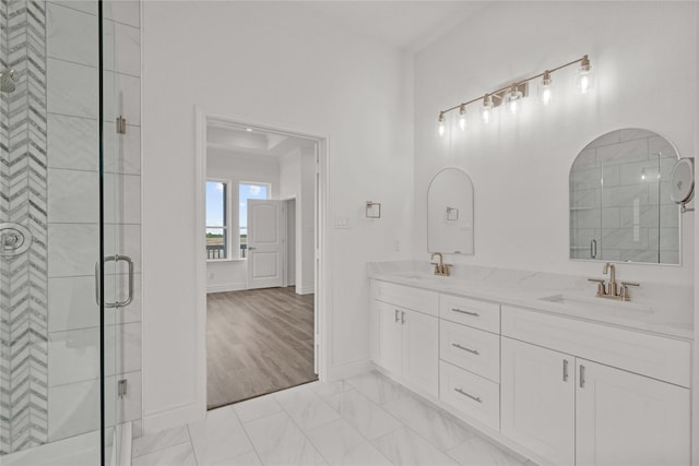 bathroom featuring a stall shower, double vanity, a sink, and baseboards