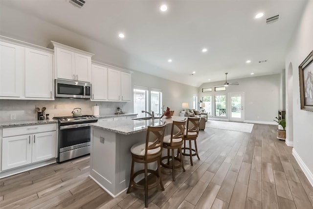 kitchen featuring an island with sink, stainless steel appliances, light wood-style floors, visible vents, and open floor plan