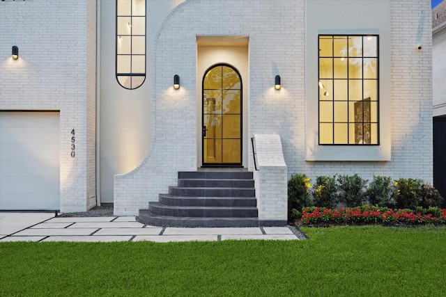 doorway to property featuring a lawn, a garage, and brick siding