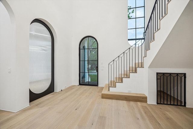 foyer with a towering ceiling, wood finished floors, stairway, and arched walkways