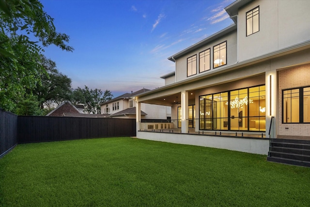 back of house with brick siding, a fenced backyard, stucco siding, and a lawn