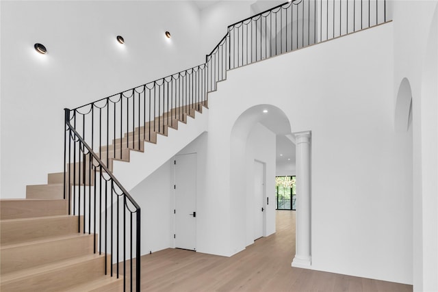 staircase with a high ceiling, arched walkways, and wood finished floors