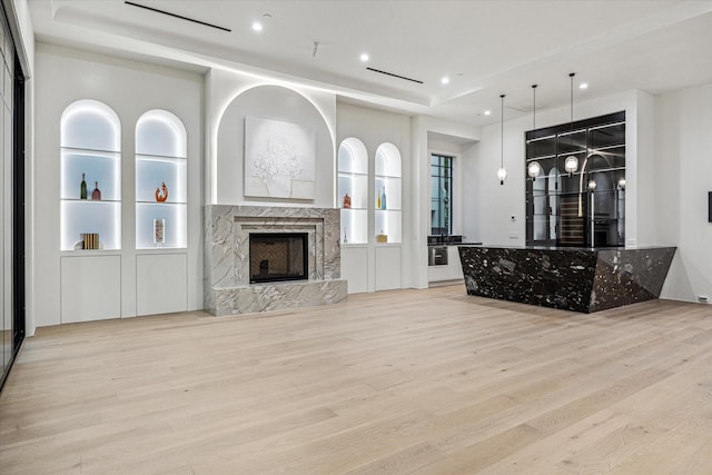unfurnished living room with recessed lighting, a high end fireplace, light wood-style flooring, and a tray ceiling