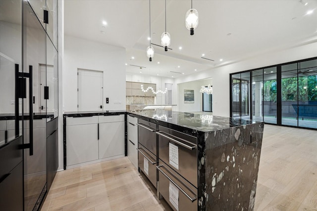 kitchen featuring light wood-style flooring, dark stone counters, white cabinetry, pendant lighting, and a peninsula