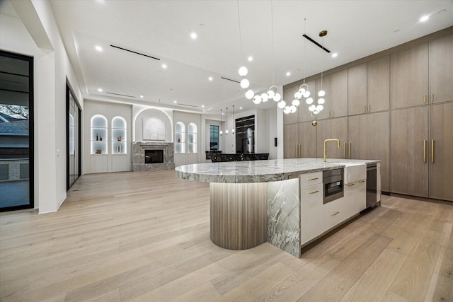 kitchen featuring open floor plan, a large island with sink, light wood-type flooring, light stone countertops, and modern cabinets