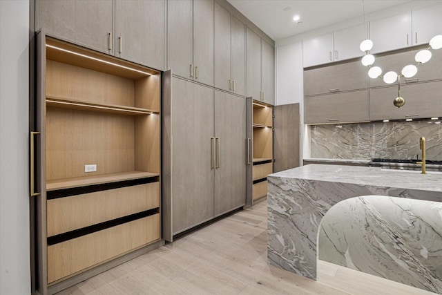 kitchen featuring light stone countertops, a sink, light wood-type flooring, backsplash, and pendant lighting