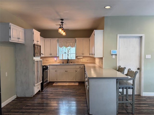 kitchen with a sink, stainless steel gas range, a peninsula, a breakfast bar, and dark wood-type flooring