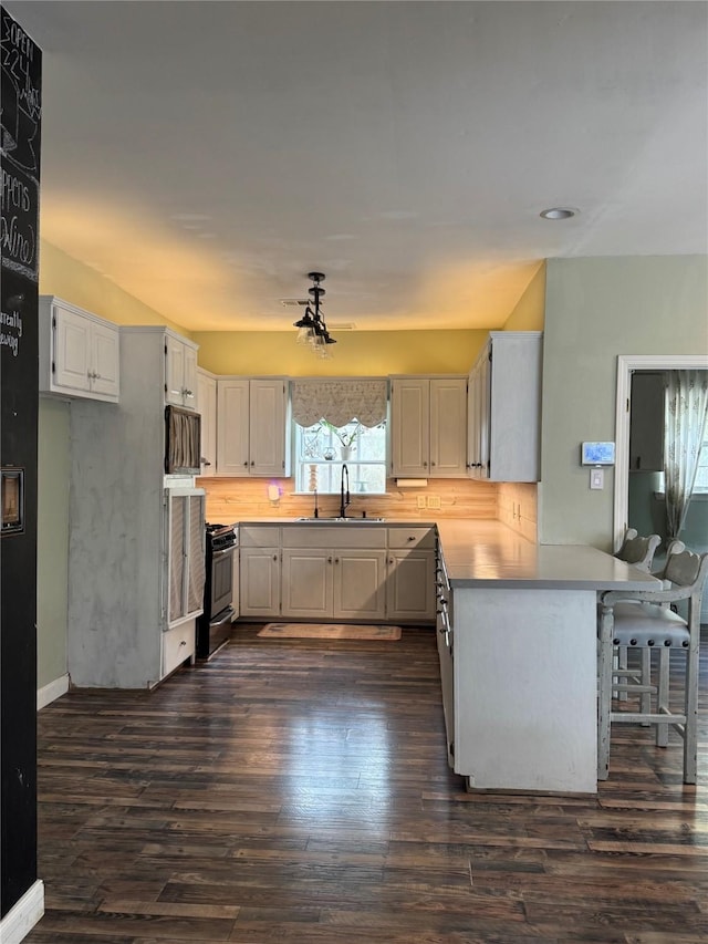 kitchen with dark wood-style flooring, a kitchen bar, a sink, a peninsula, and gas range oven