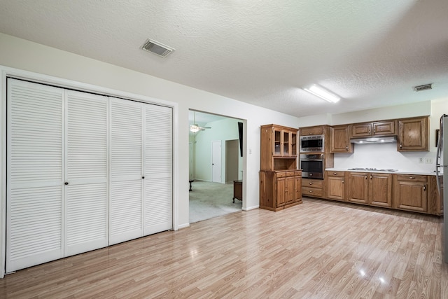 kitchen with appliances with stainless steel finishes, visible vents, light wood finished floors, and under cabinet range hood