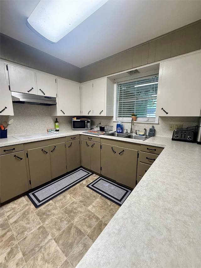 kitchen featuring a sink, under cabinet range hood, light countertops, and stainless steel microwave